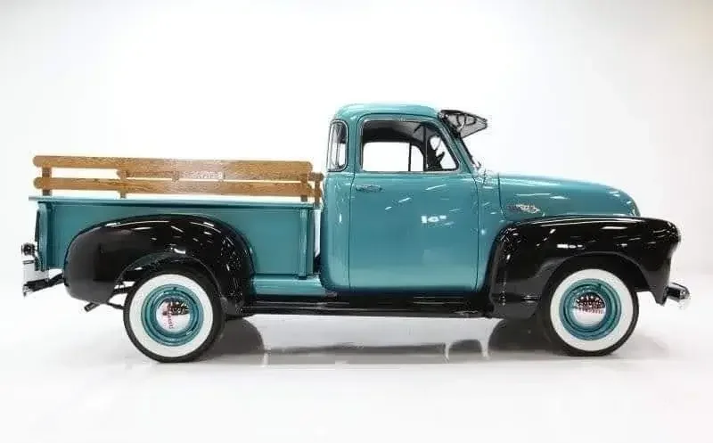 Vintage blue pickup truck with black fenders and whitewall tires, wooden bed sides, and a black bumper.
