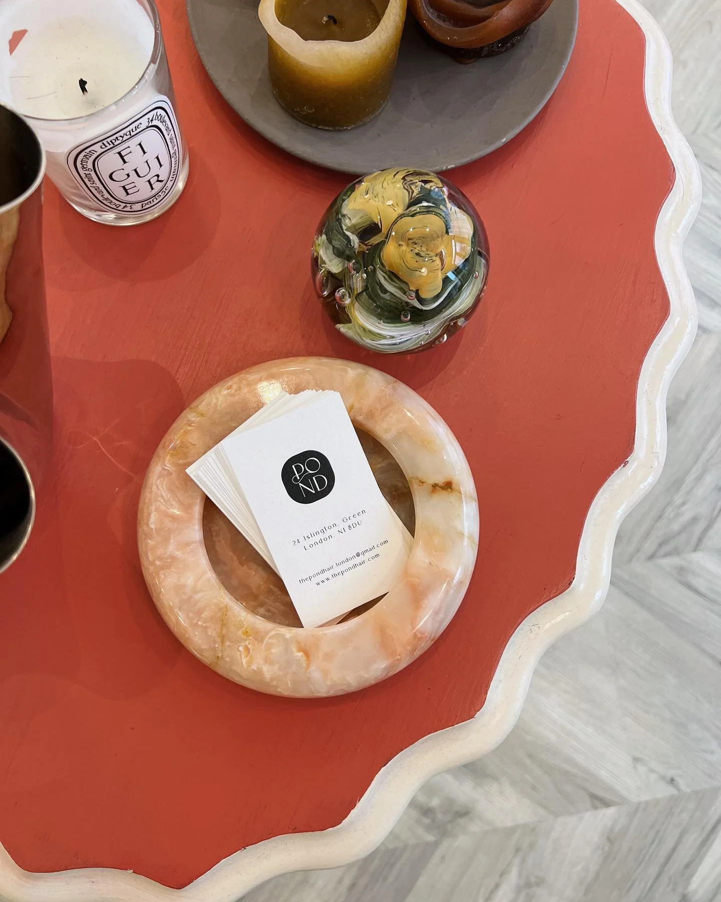 A decorative table with colorful candles, a business card in a marble ring holder, and a multicolored glass paperweight.