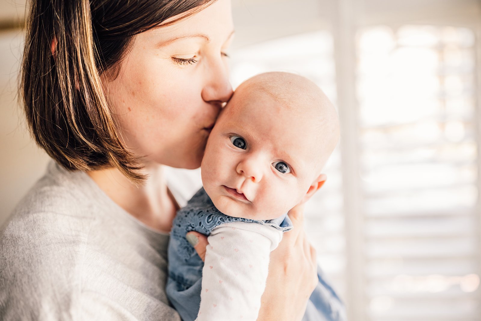 Mother kissing baby on the head while holding the child in her arms, with soft lighting in the background.