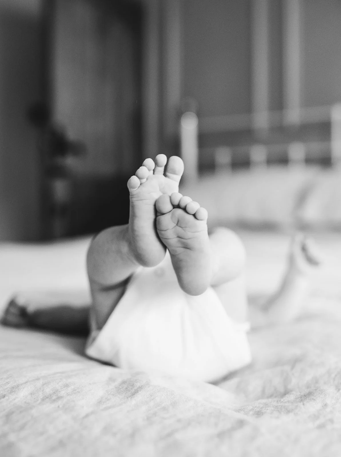 Black and white photo of a baby's feet in the air on a bed.