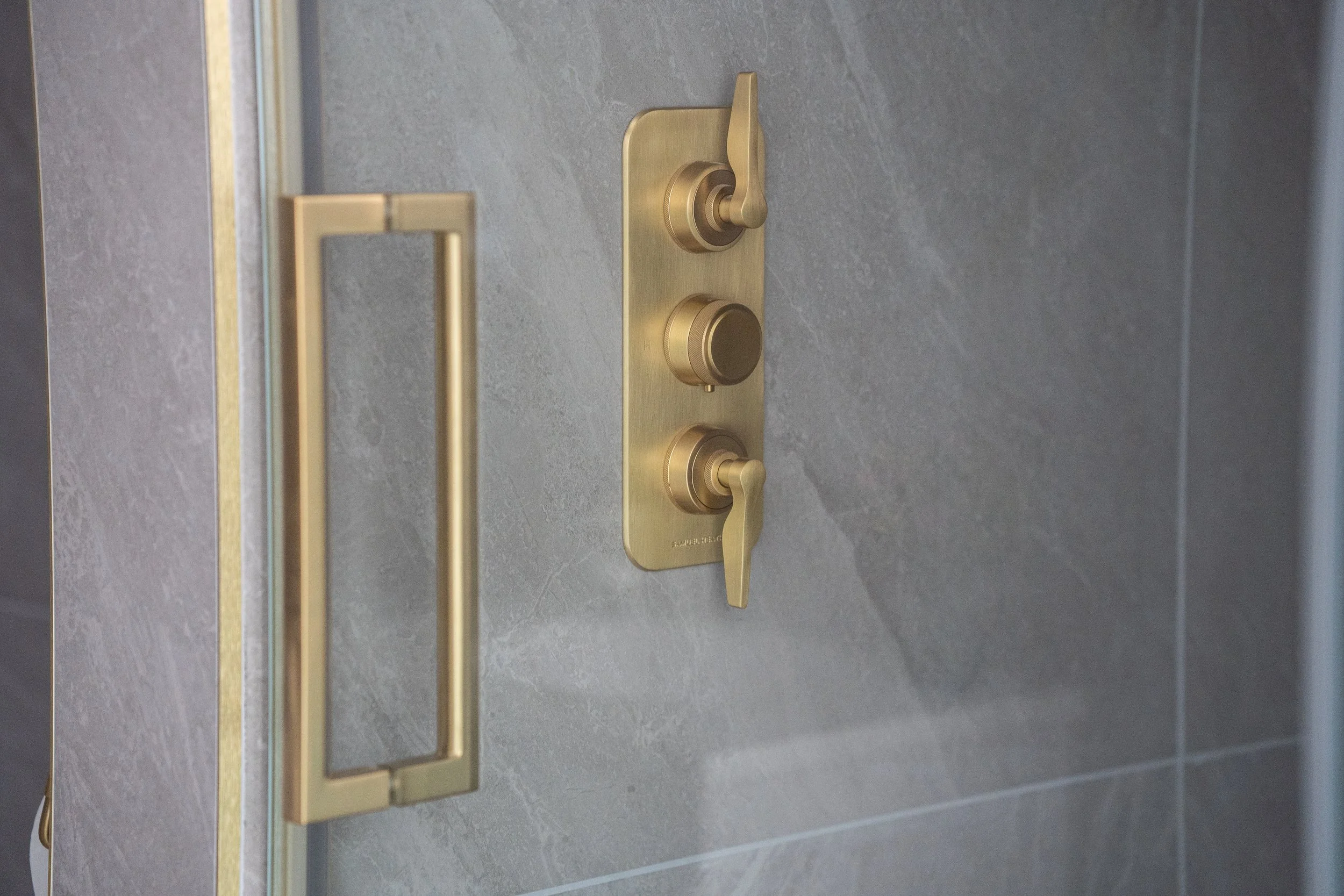 Close-up of a modern gold-colored door handle with a lever, a turn lock, and a lock knob on a gray tiled door.