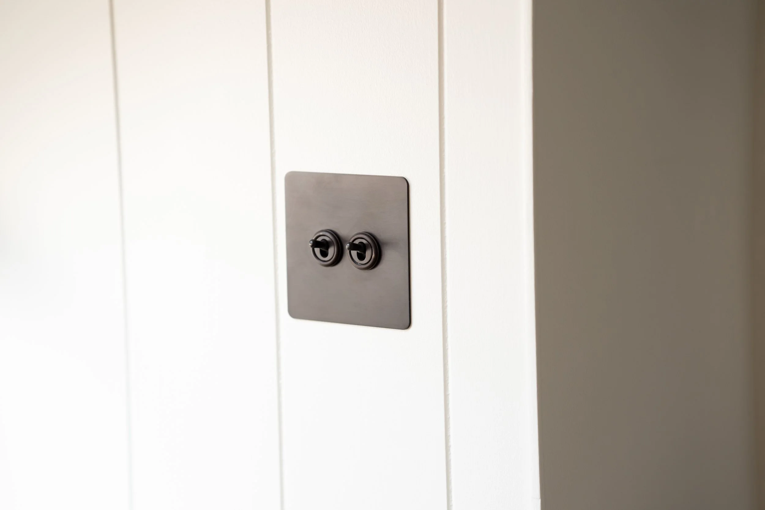Close-up of a metallic double light switch on a white wooden-paneled wall.