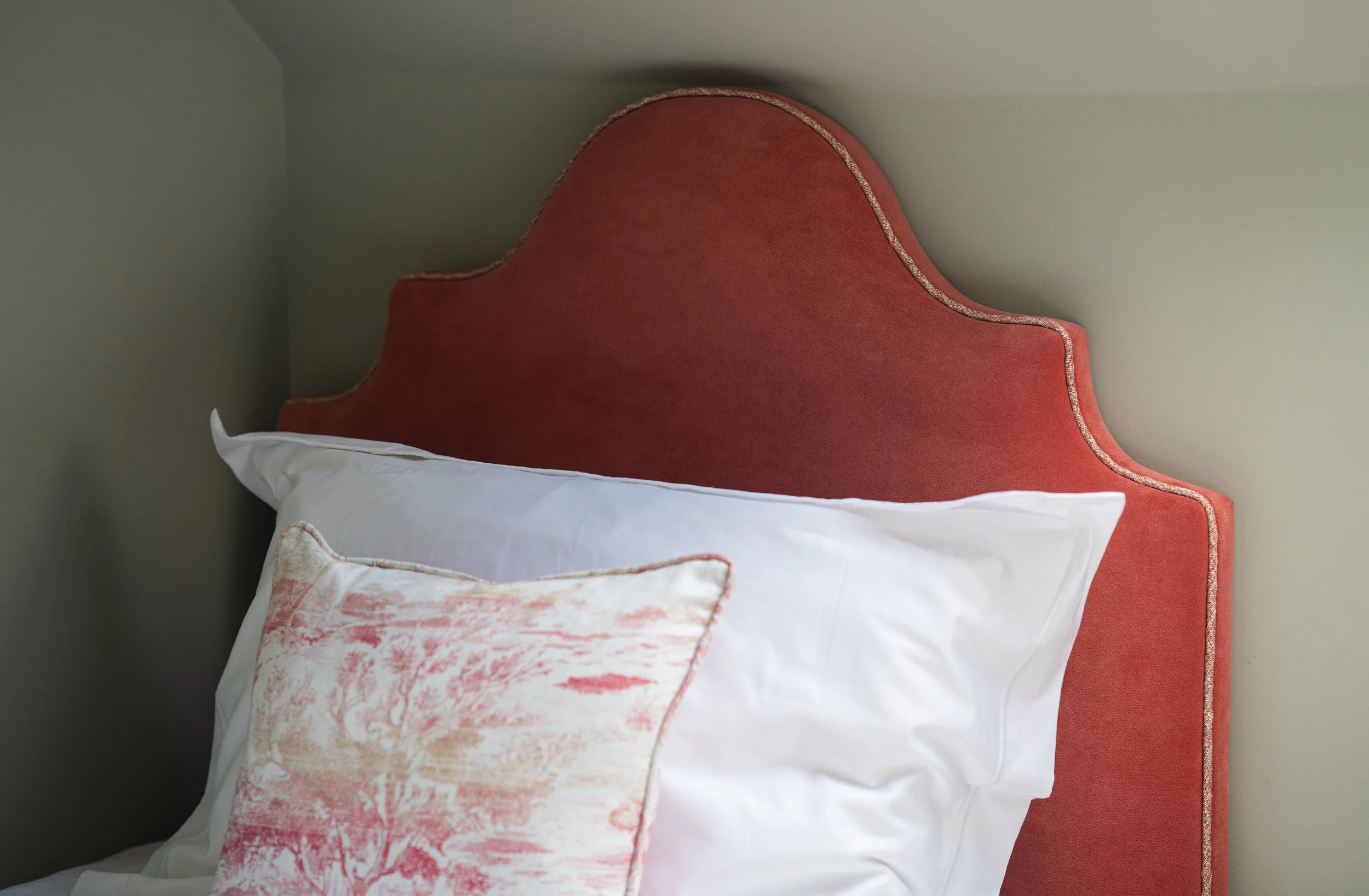 Close-up of a bedroom headboard with white pillows and a decorative pillow in front, against a beige wall.