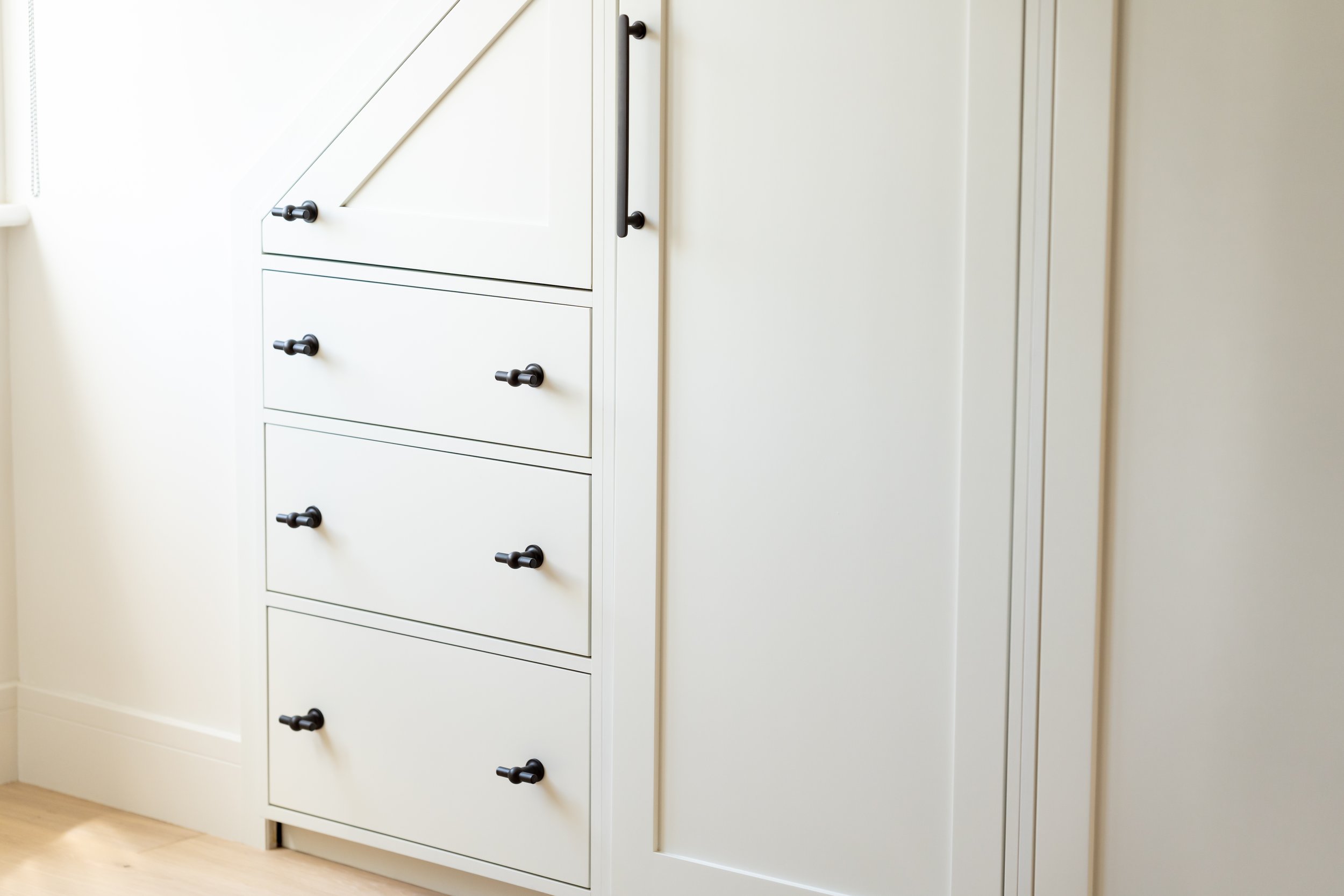 White built-in cabinet with black knobs in a room with hardwood floor.