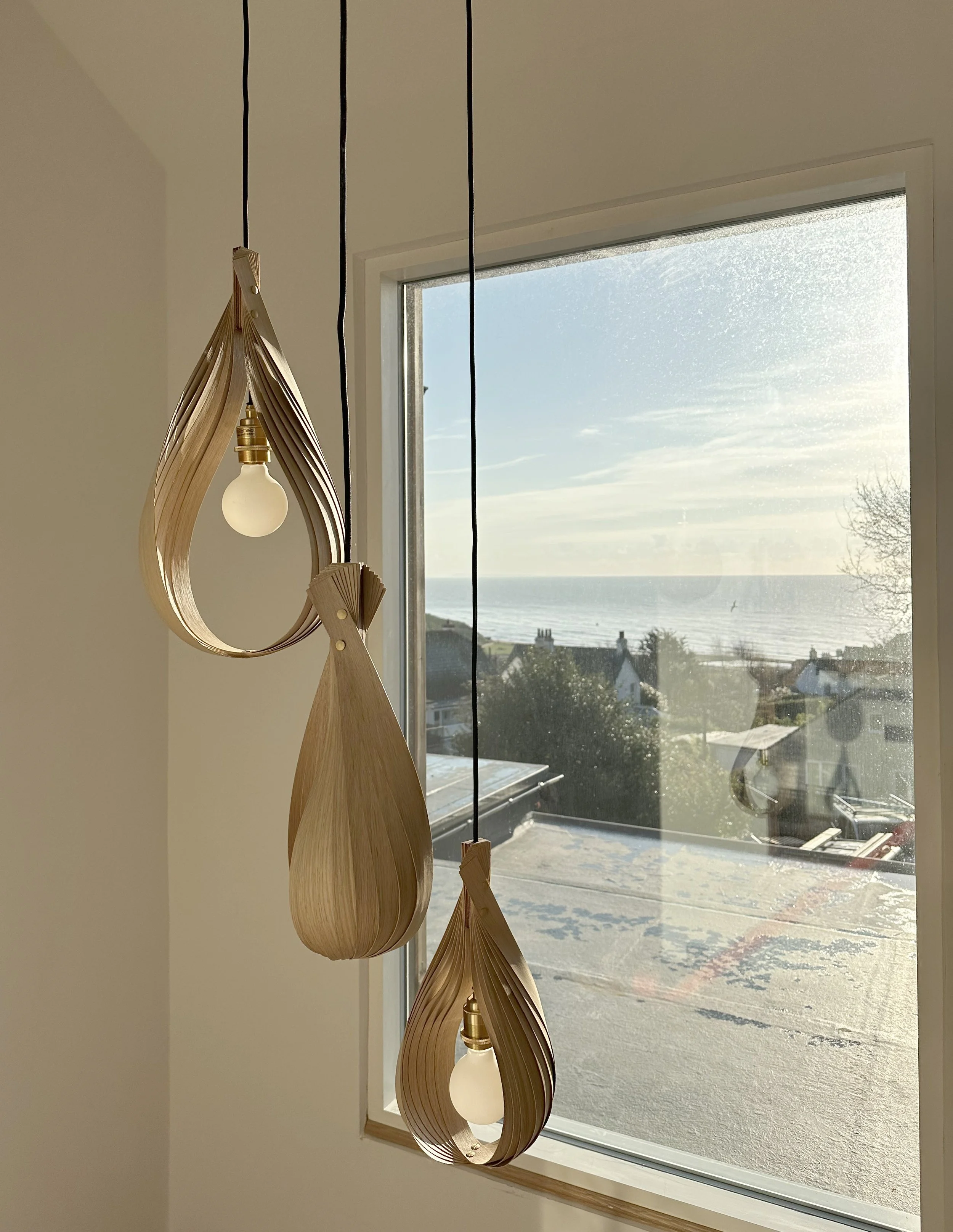 Decorative wooden pendant lights hanging by a window with a seaside view.