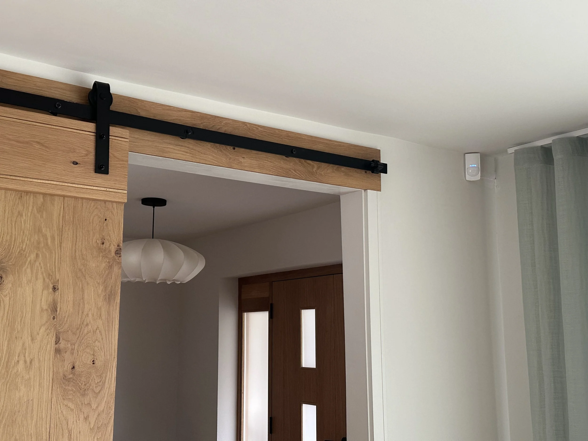 Interior view of a room with a sliding wooden barn door, black hardware, a modern pendant light, and a window with light green curtains.