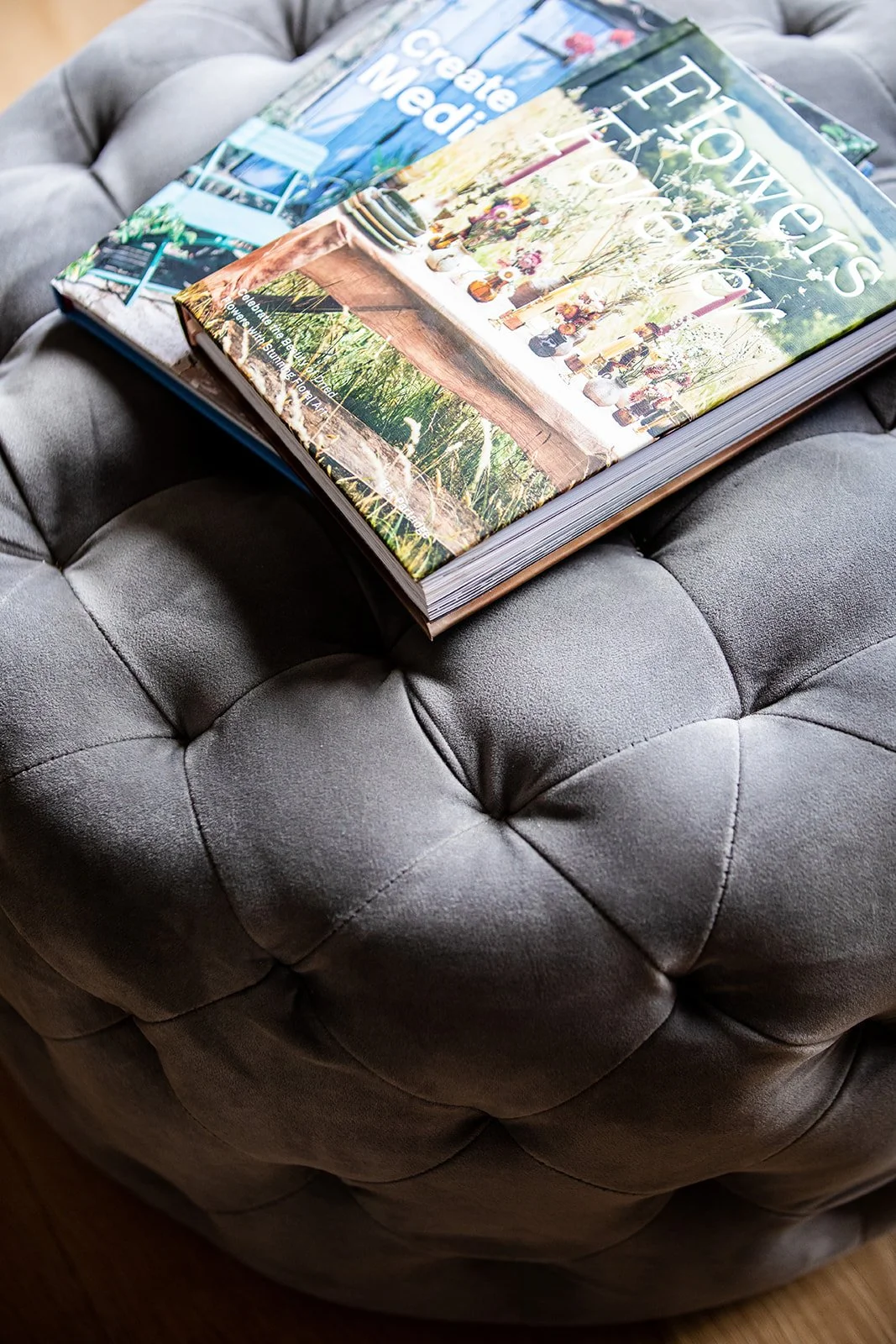 Three open magazines on a gray tufted ottoman, featuring content about flowers, home design, and creating media.