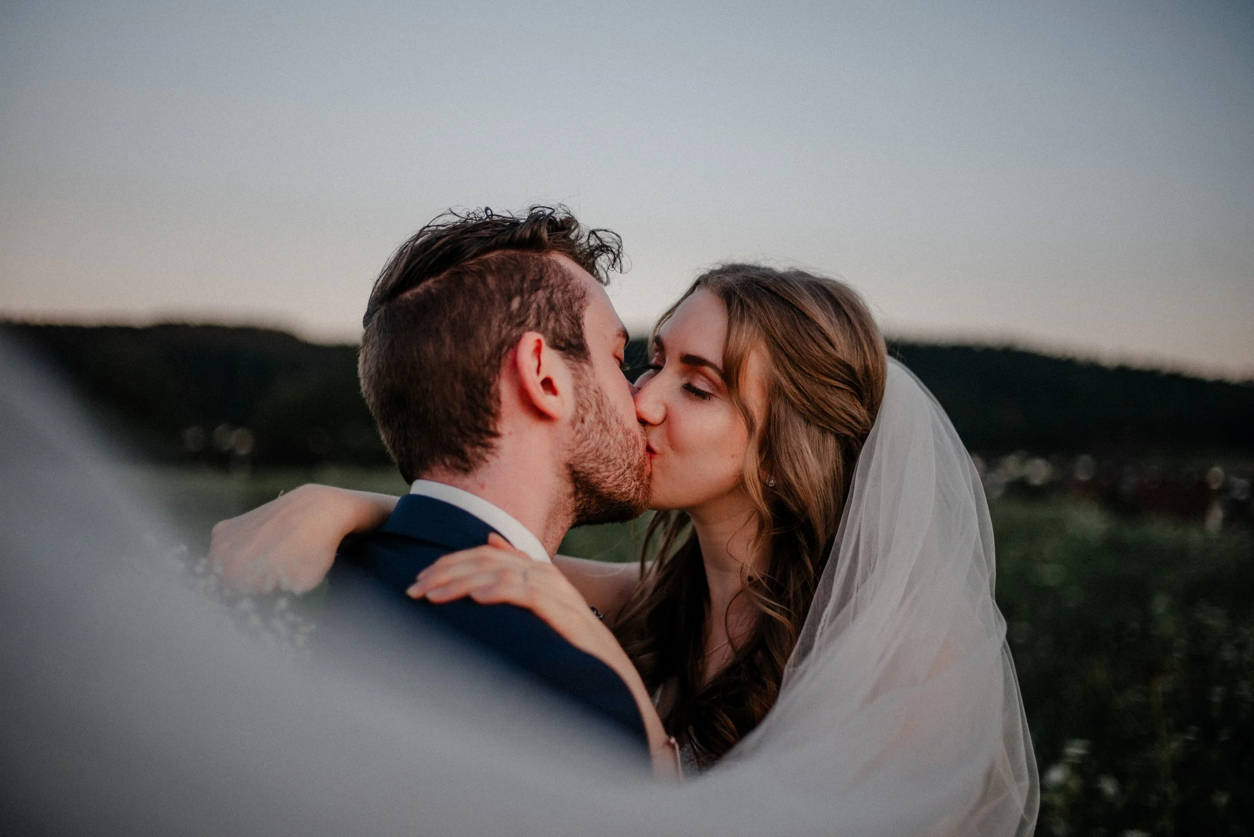 Ein Brautpaar küsst sich bei Sonnenuntergang im Freien.