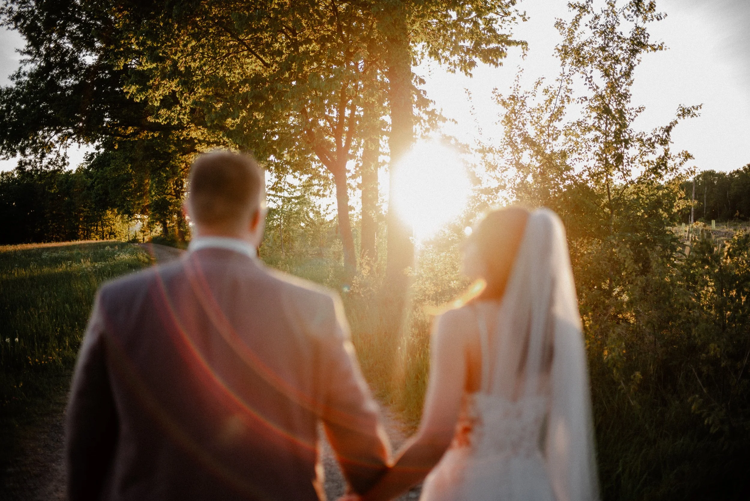 Ein Brautpaar, das sich an einem Sonnenuntergang hält, im Freien umgeben von Bäumen, bei ihrer Hochzeit.