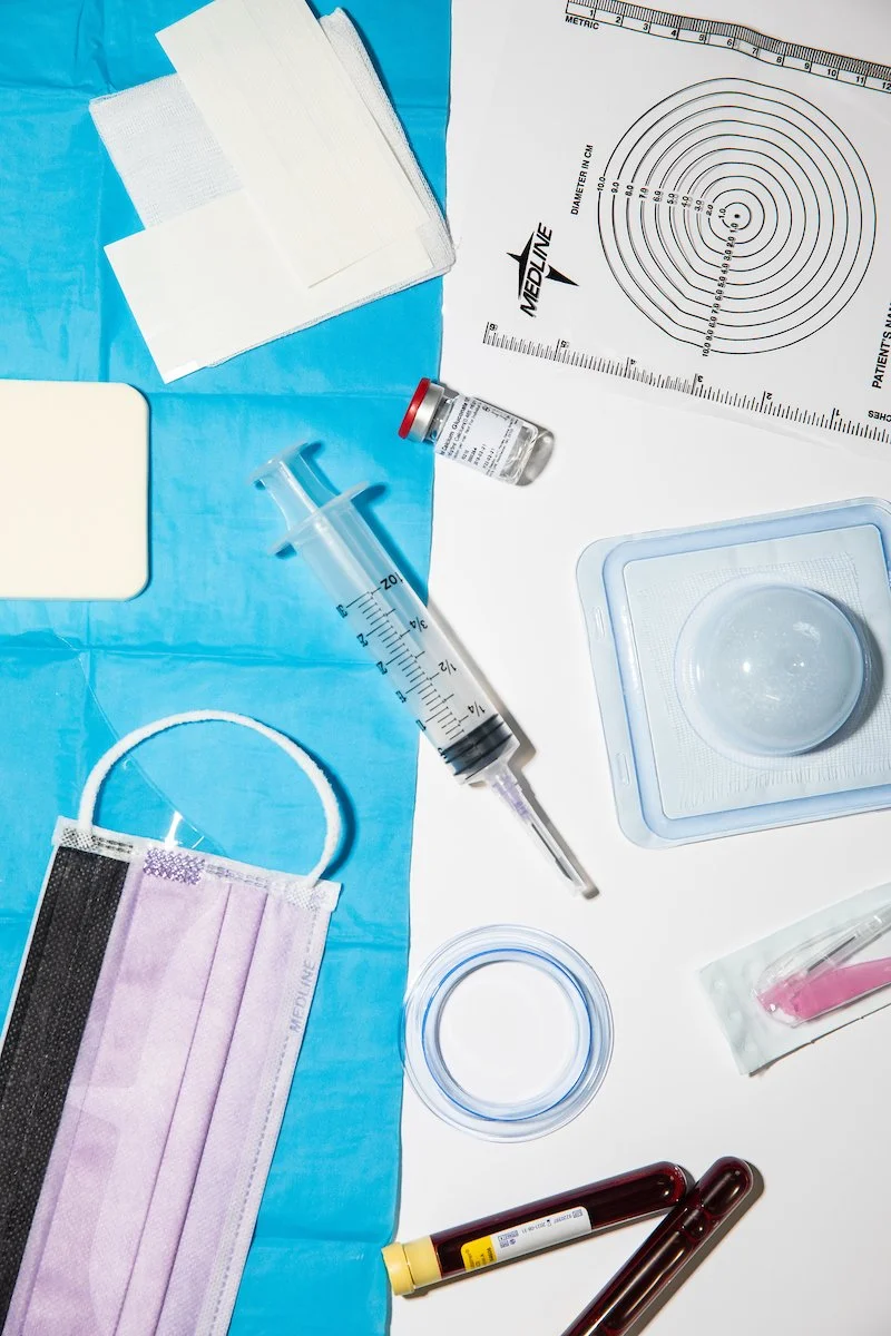 Medical supplies including syringe, vial, face mask, test tubes, and wound measurement chart on blue and white background.