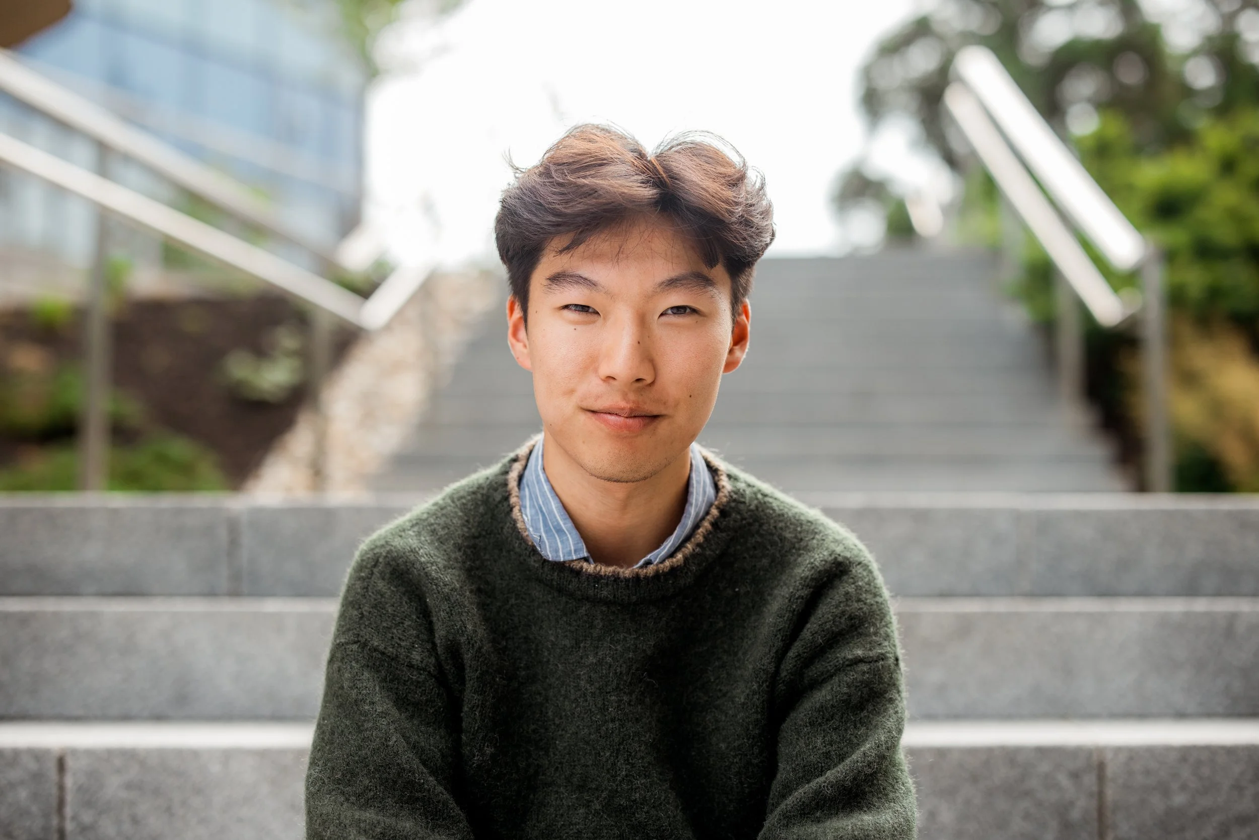Young person sitting on outdoor steps, wearing a green sweater.