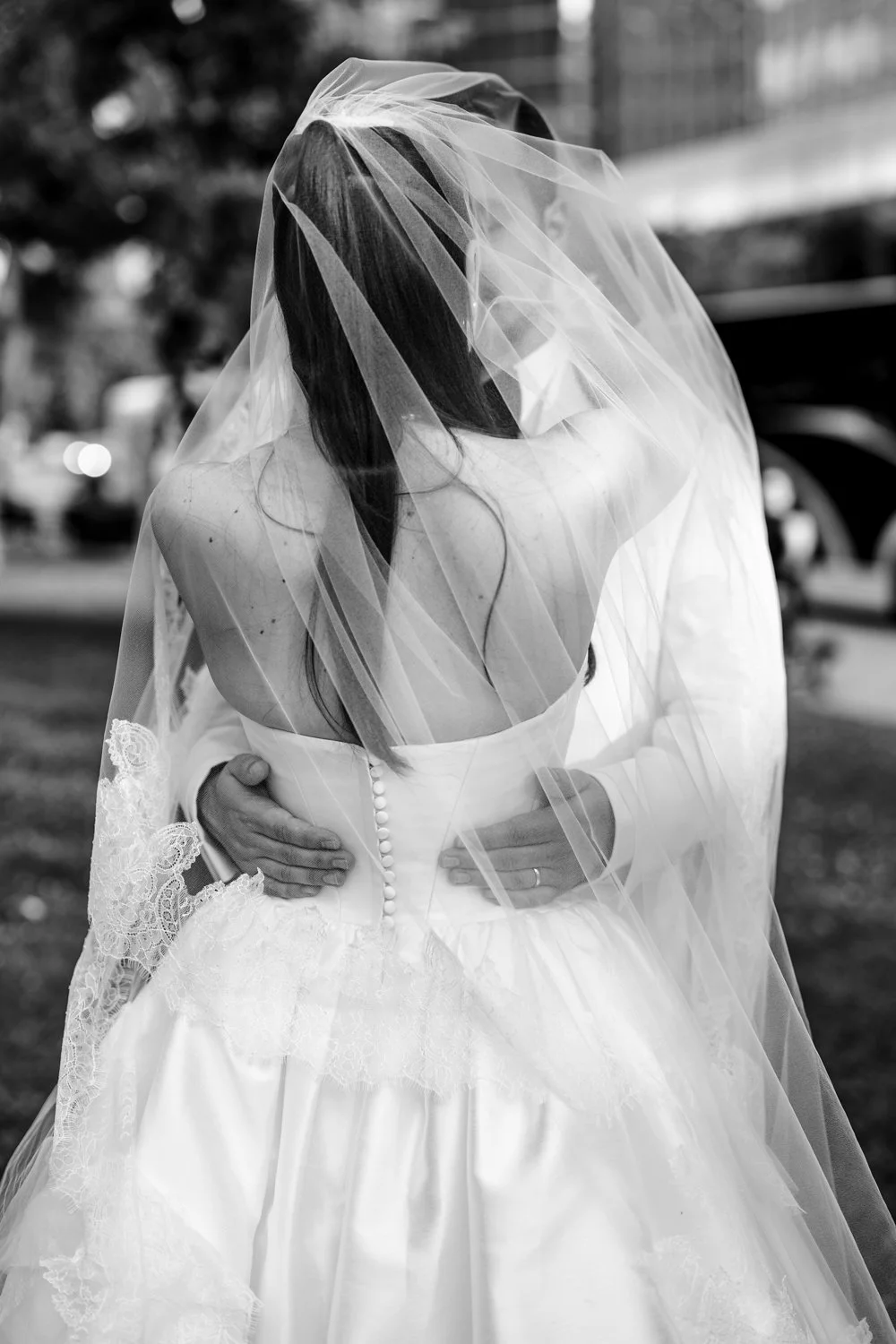 Artistic black and white portrait of a bride and groom embracing beneath the bridal veil on their wedding day.