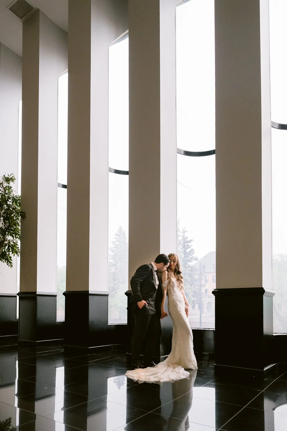 Bride and groom sharing a romantic portrait in front of the dramatic floor-to-ceiling windows at Plaza Antique in Montreal on their wedding day.