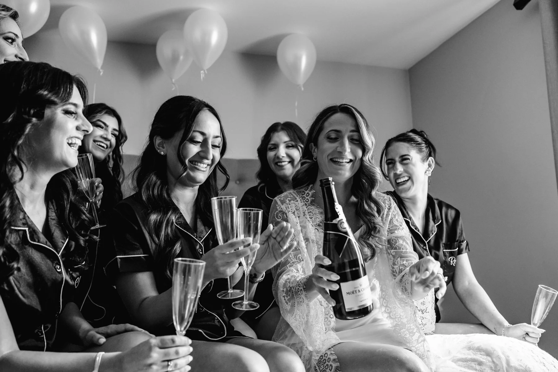 Bride and her bridesmaids having champagne before getting dressed on the wedding day