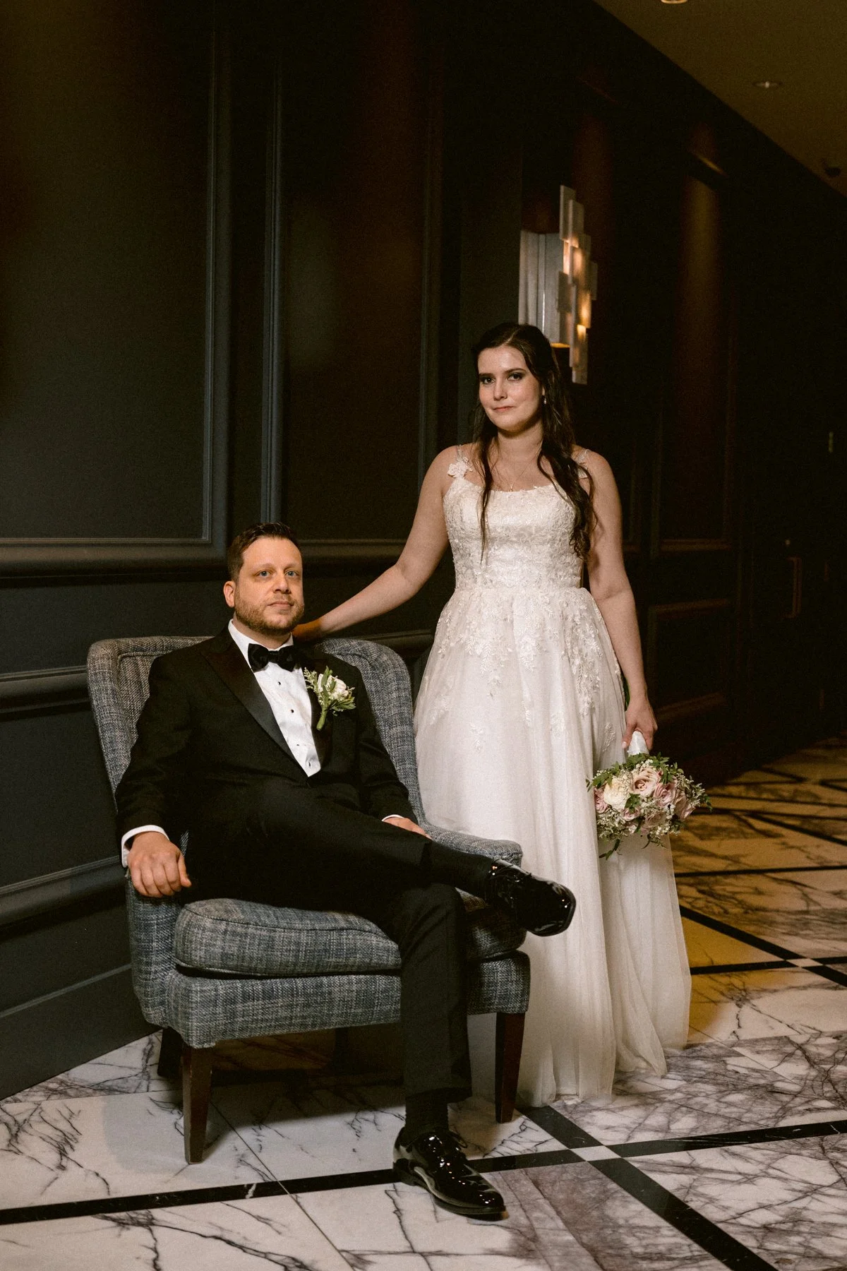 Bride standing beside groom seated in an armchair at Golf Metropolitain in Montreal on their wedding day