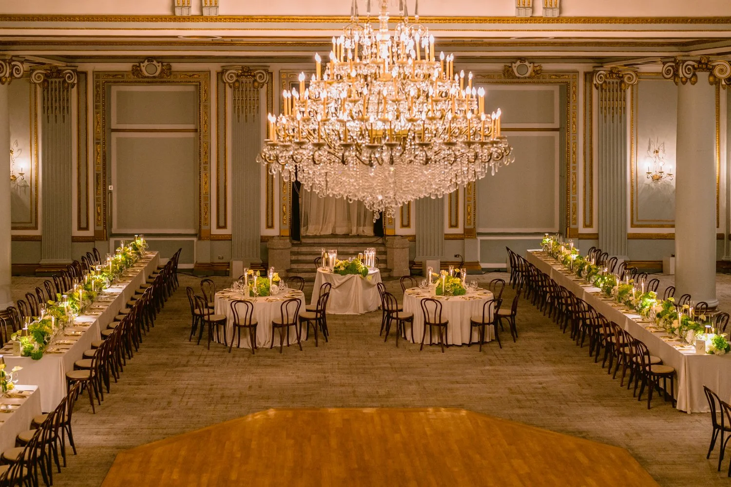 Elegant wedding reception setup at Le Windsor in Montreal featuring long banquet tables, candlelight, lush floral arrangements, and a crystal chandelier.