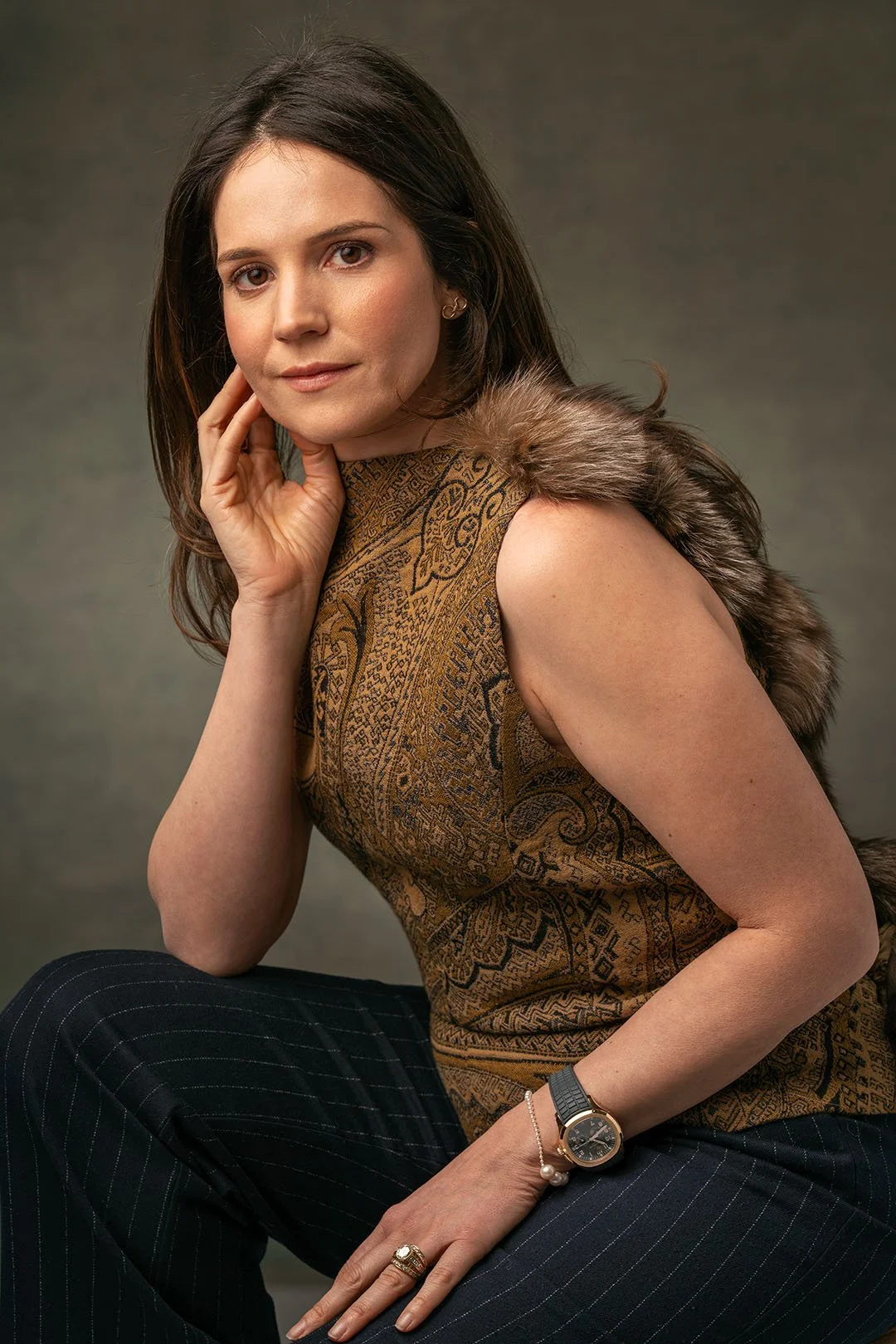 This professional headshot, taken by a Montreal-based portrait and headshot photographer, showcases a poised woman in an elegant studio portrait. She wears a patterned golden-brown top with a fur accent and pinstriped trousers, exuding confidence aga