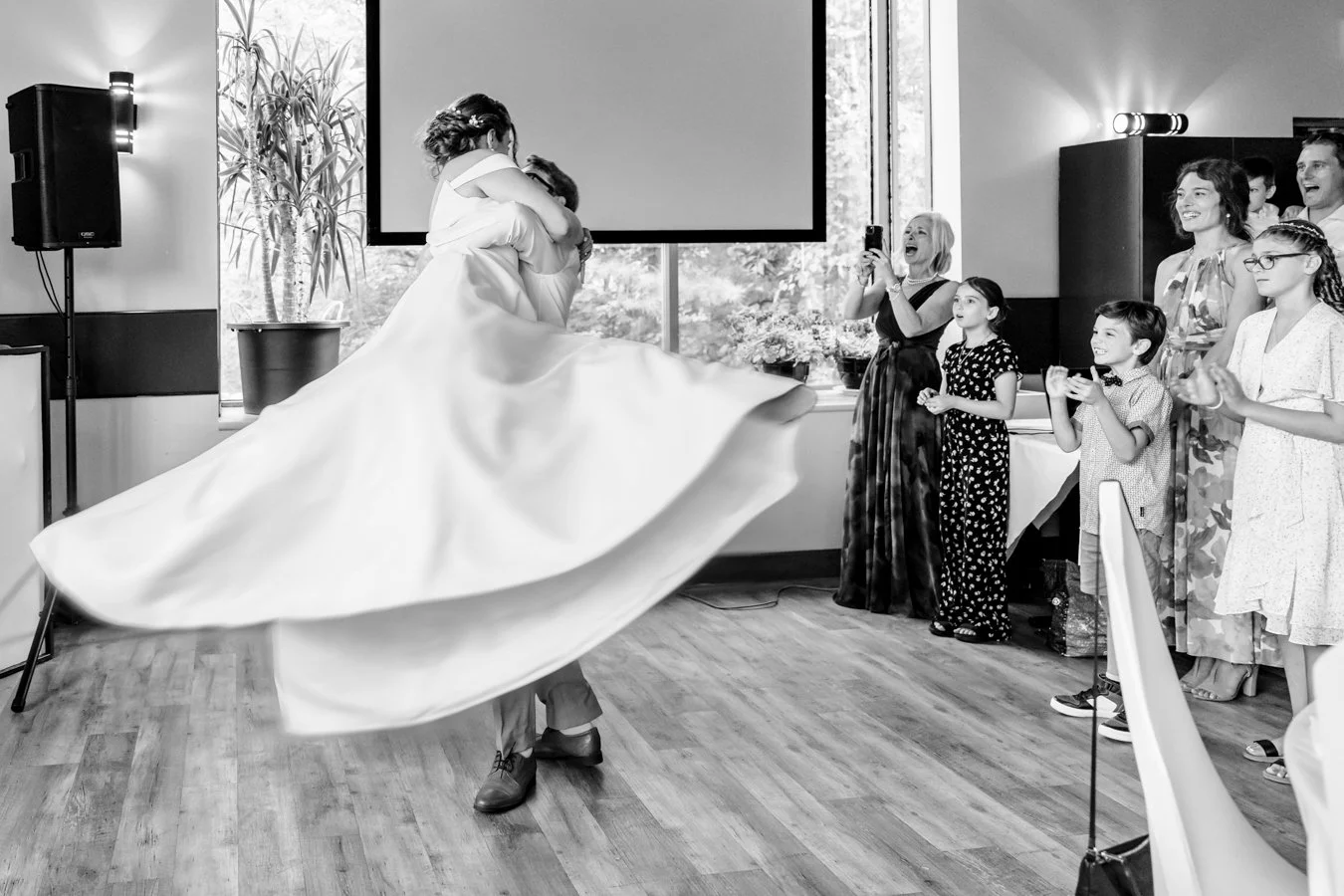 couple first dance at auberge Val-St-Come. Groom lifting bride and her dress twirls while family watch in awe