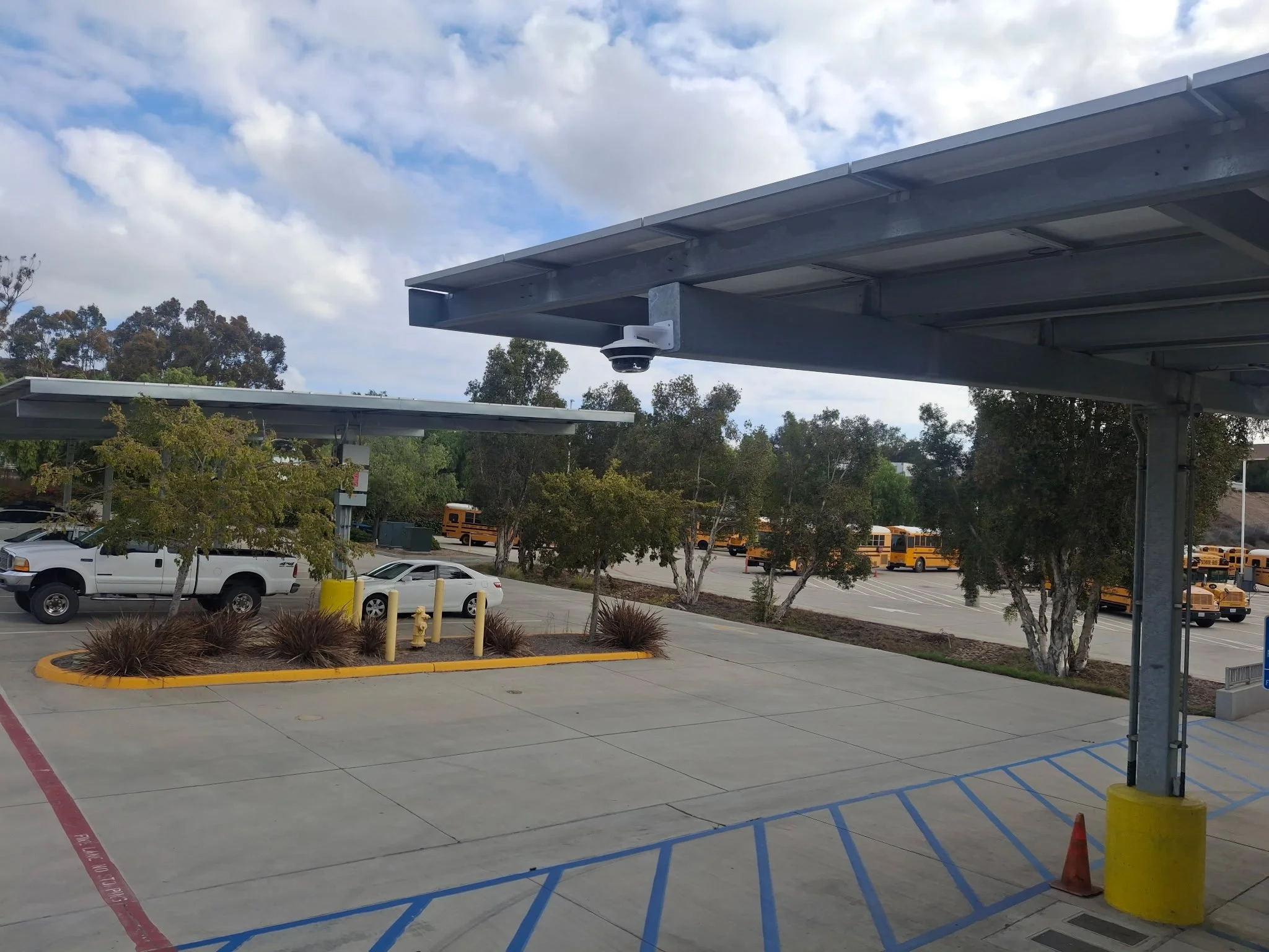 A parking lot with cars, trees, and a cloudy sky, featuring a structure with a surveillance camera attached.