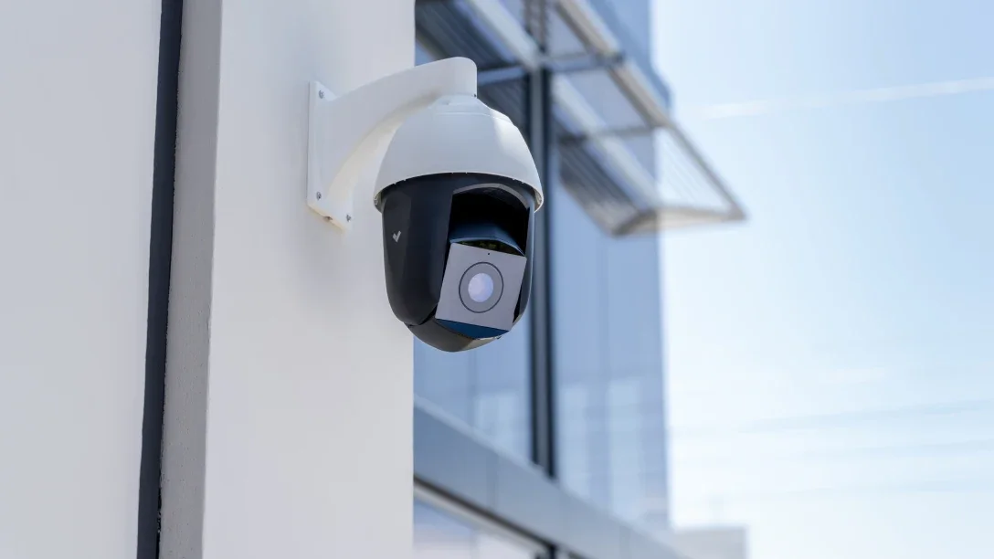 Security camera mounted on a white wall outside a modern building with glass windows.