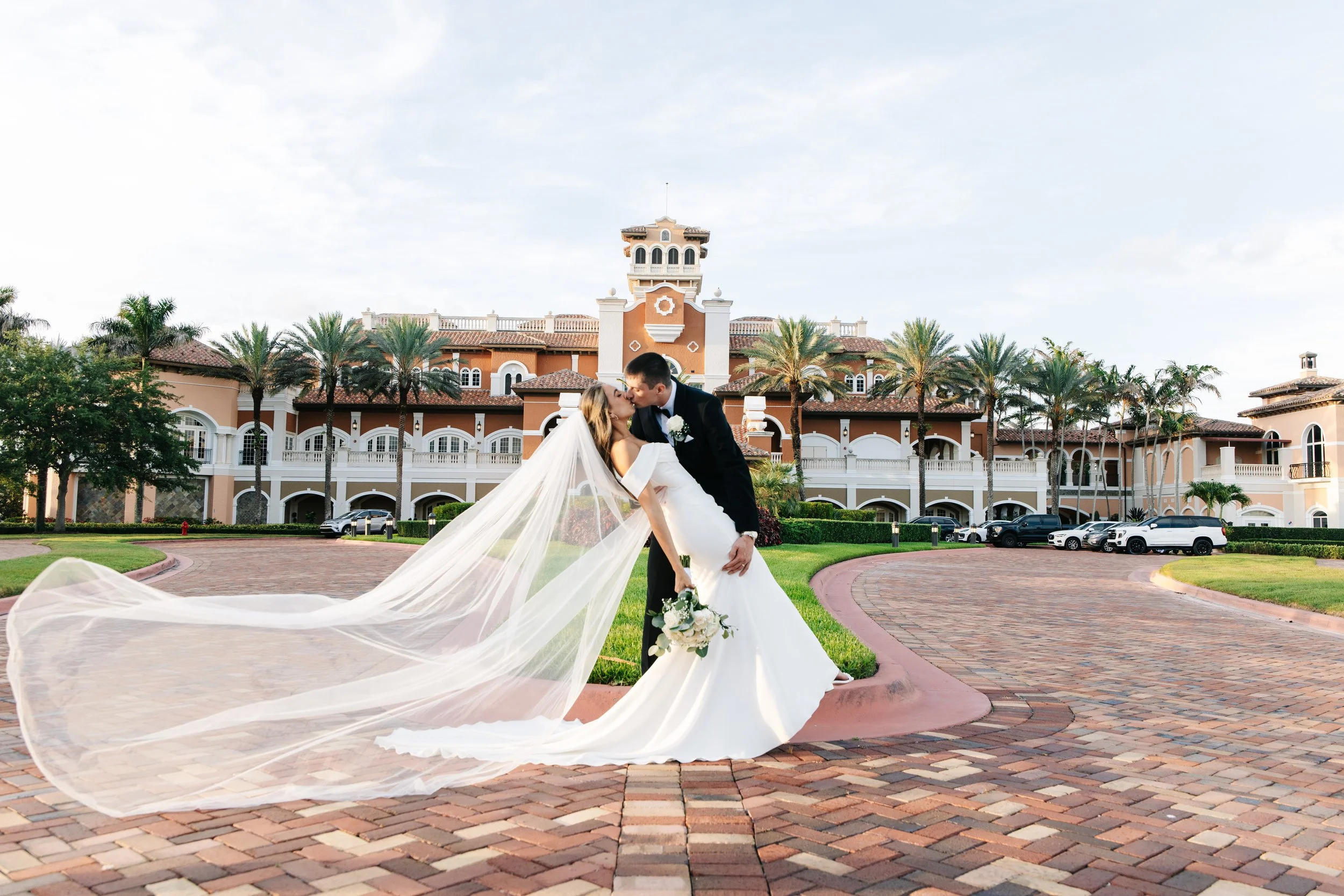  Bride and groom posing outside an elegant Palm Beach wedding venue with the bride’s veil flowing 