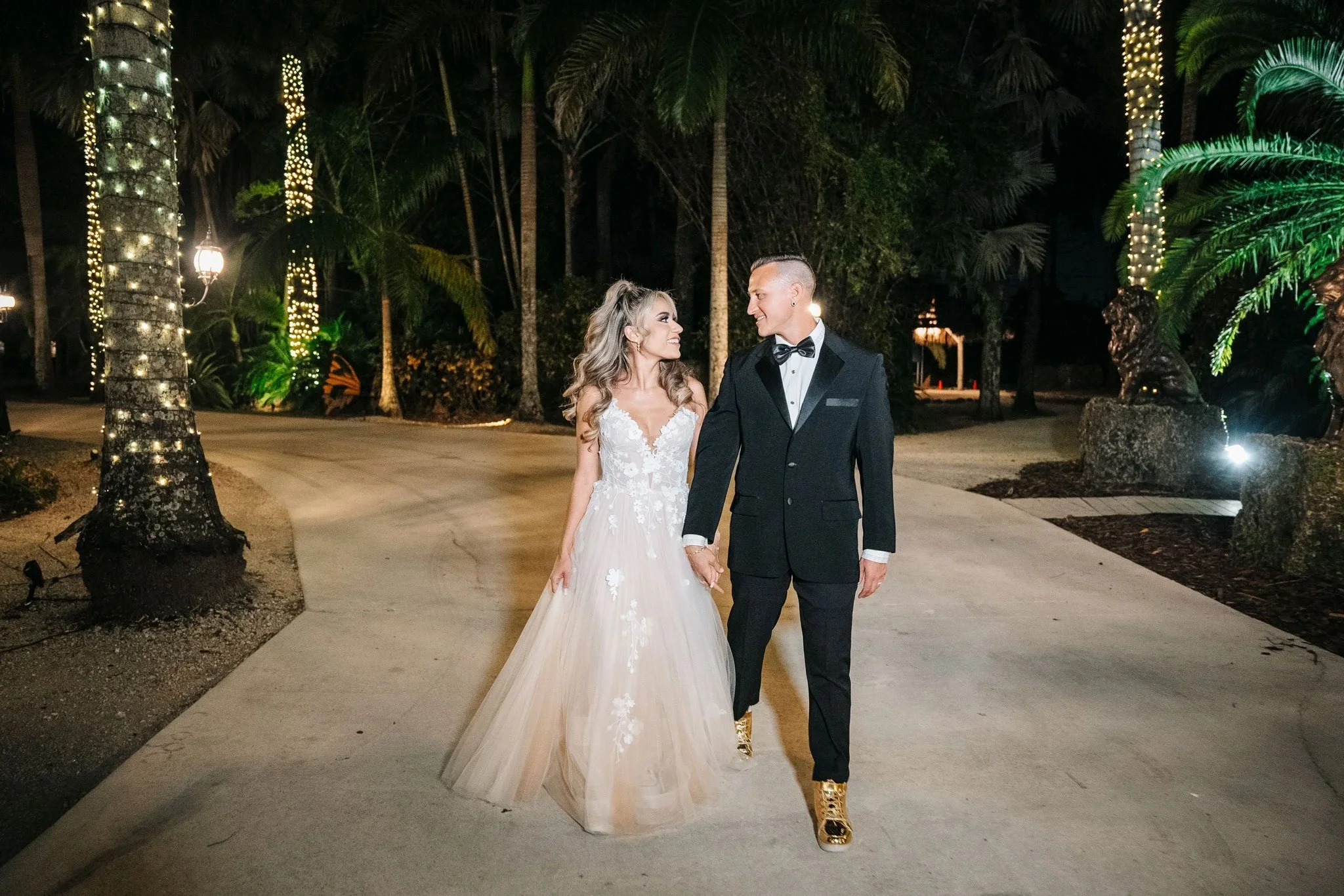 Newlywed couple walking beneath illuminated palm trees at Secret Gardens Miami at night