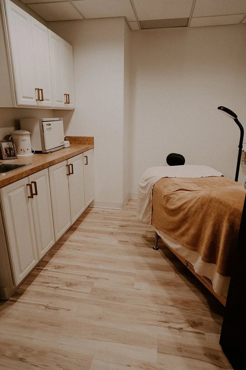 Facial suite with a bed covered in a tan blanket, a white pillow, a black headrest, and a black adjustable lamp  at Salt + Light Salon and Spa in Cincinnati, OH