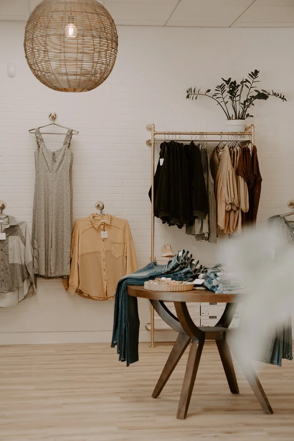 Display of women's clothing in a boutique, including dresses, shirts, and jackets, with a wooden table showcasing folded jeans at the Shop Salt boutique.