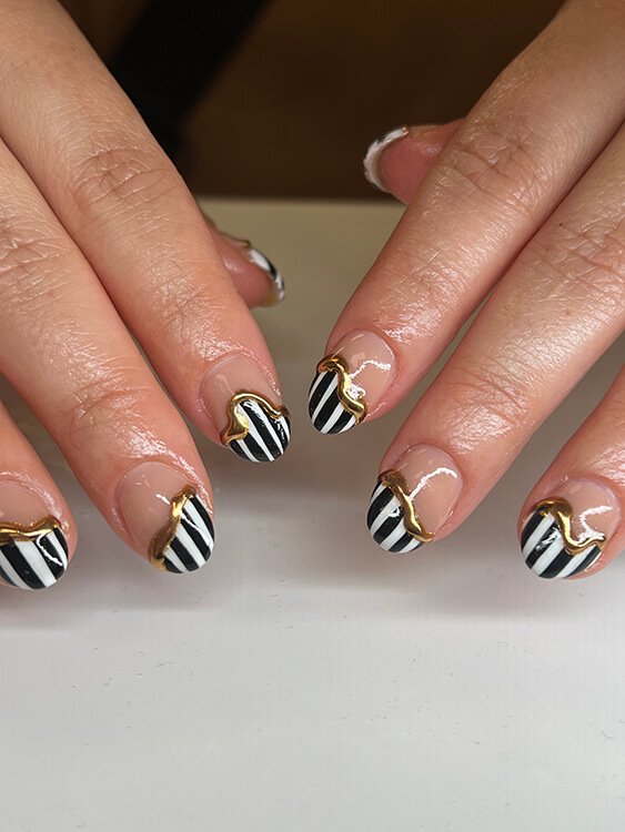 Custom nail art with black and white striped nail art accented with gold lining done at Salt + Light Salon and Spa in Cincinnati, OH