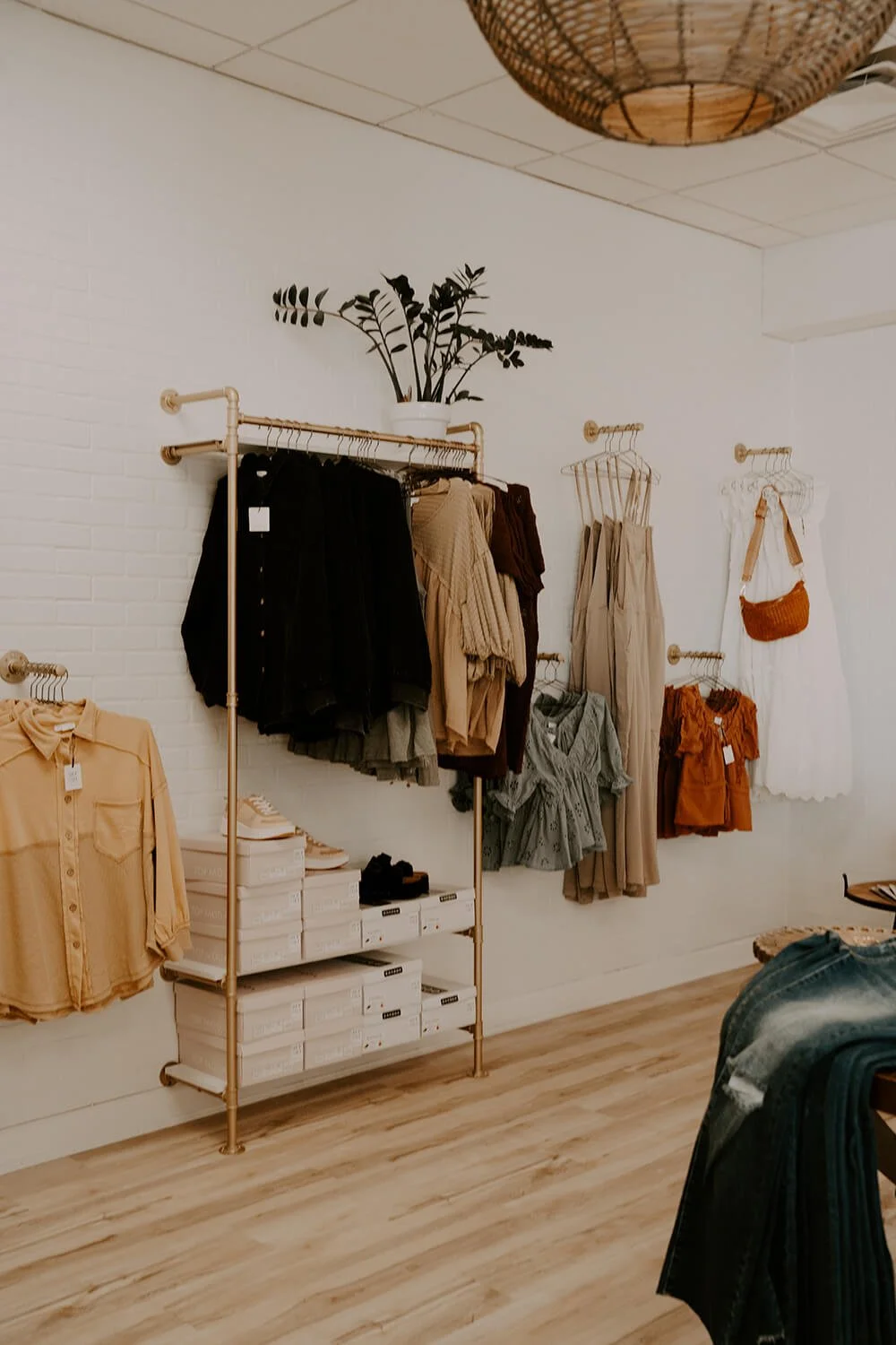 Shop Salt boutique display with hanging garments, a potted plant, and a woven ceiling light fixture.