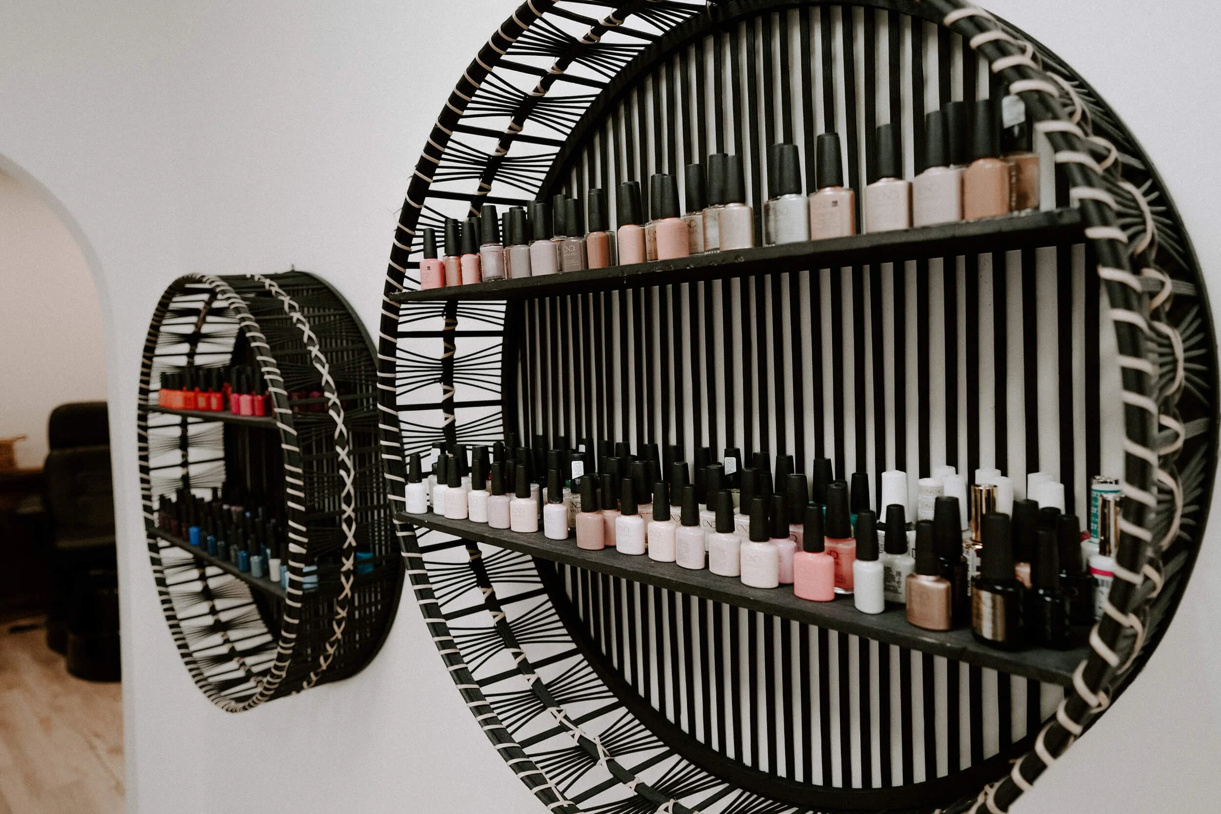 Three black round wall shelves with a striped white and black pattern, holding various bottles of nail polish in different shades  at Salt + Light Salon and Spa in Cincinnati, OH