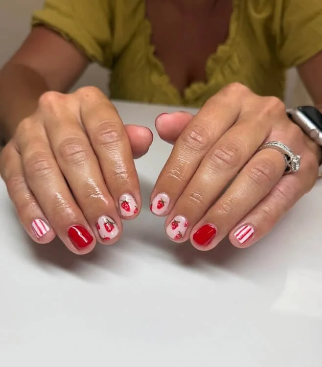 Custom nail design with red and white strawberry-themed nail polish on fingernails, resting on a white surface done at Salt + Light Salon and Spa in Cincinnati, OH