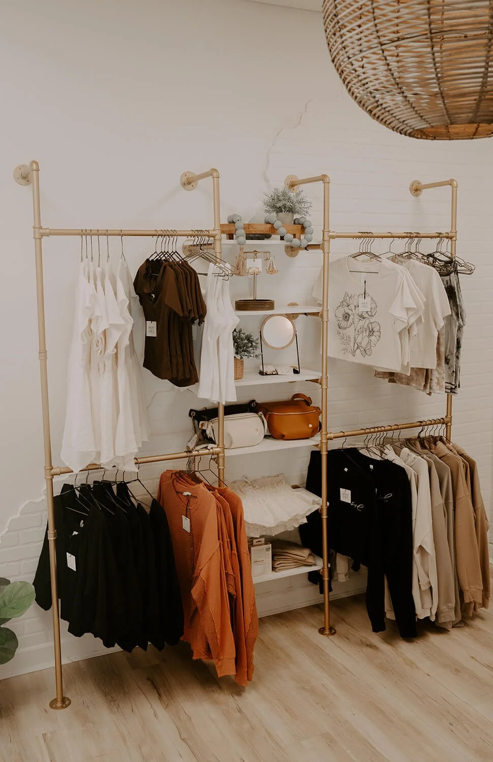 Clothing rack in a boutique with white, brown, and beige garments, decorative items, bags, and a rattan light fixture at the Shop Salt boutique.