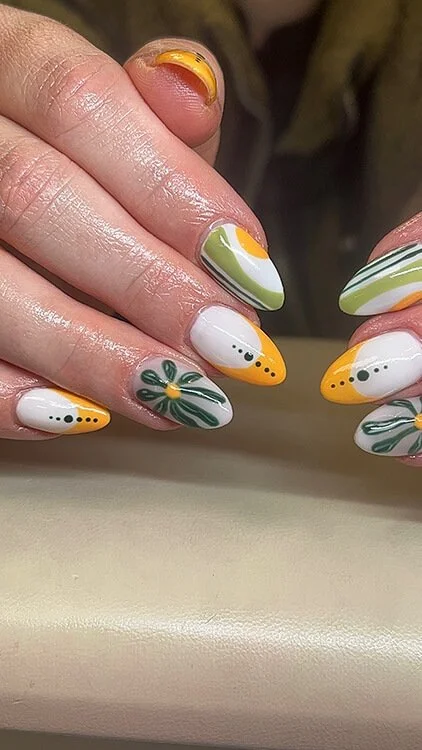 Custom nail art with colorful Easter-themed designs. Some nails feature yellow chick faces, others have white backgrounds with green leaves, and a few have abstract green, yellow, and white swirl patterns done at Salt + Light Salon and Spa