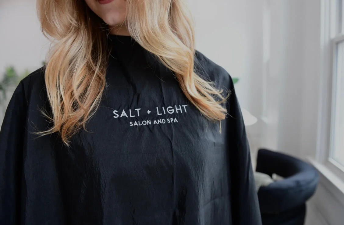 Woman wearing Salt + Light salon cape during hair styling