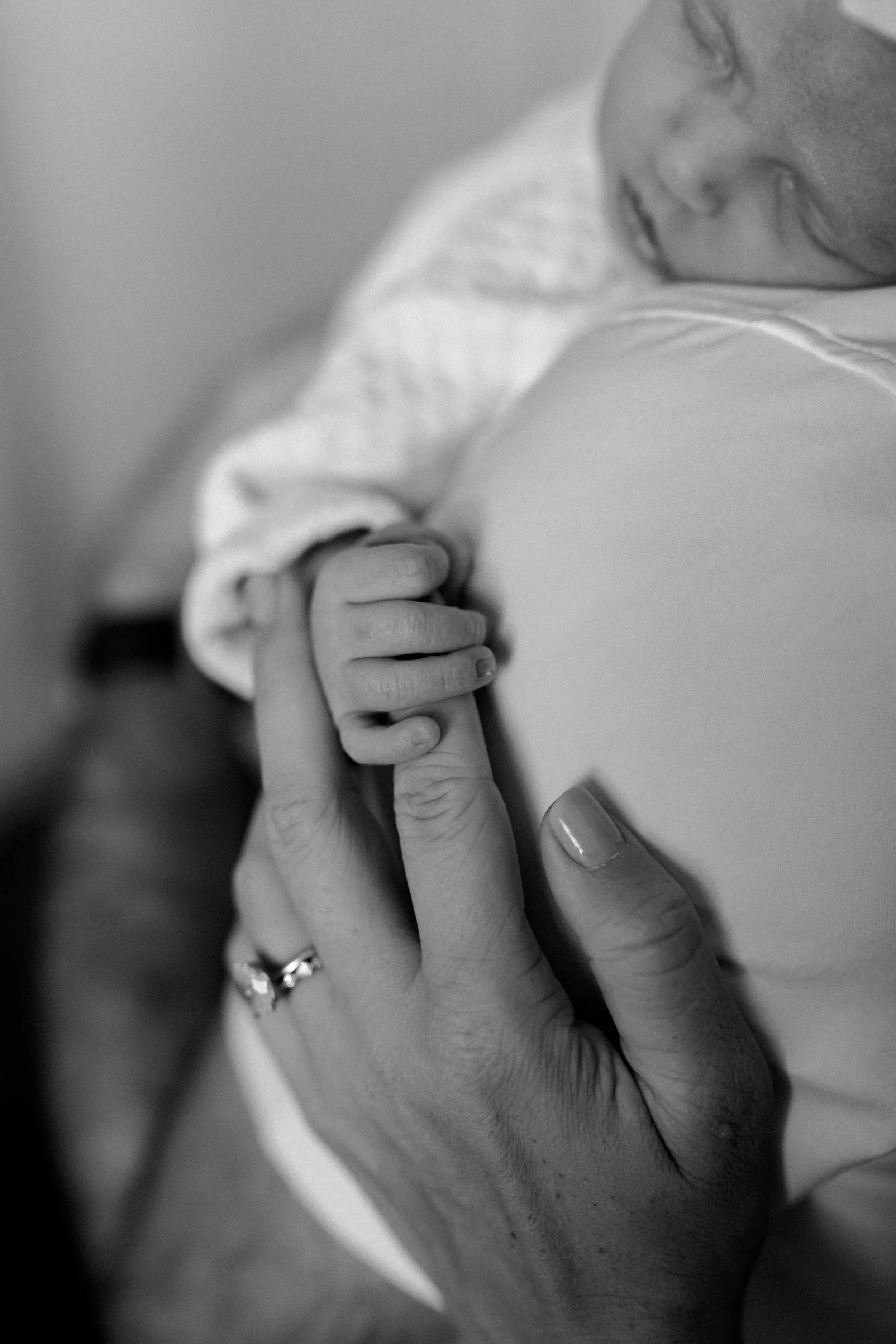 A baby holding an adult's finger, close-up black and white photograph.