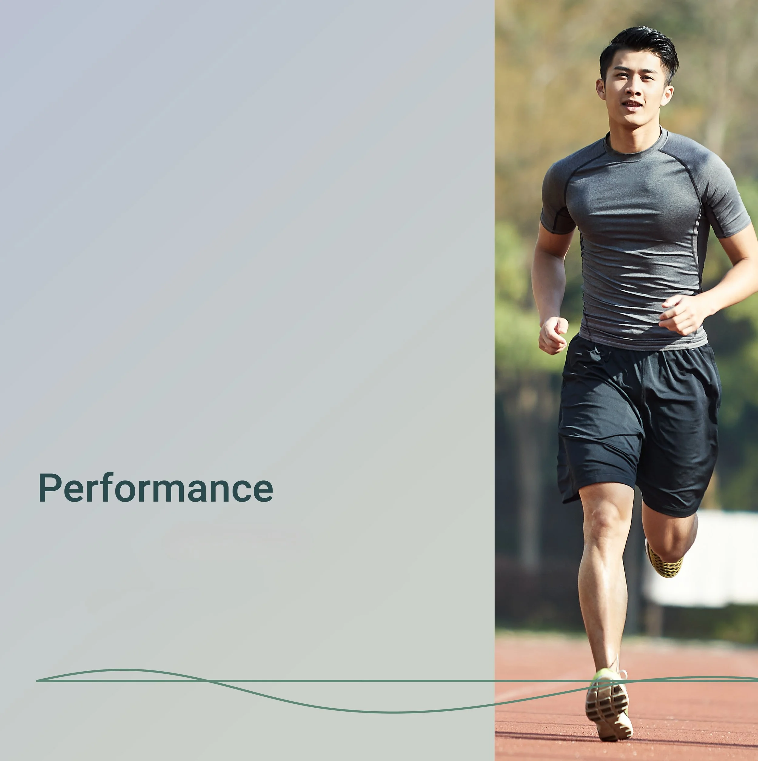 Young man jogging outdoors on a track with green grass and trees in the background, wearing a gray athletic shirt and black shorts.