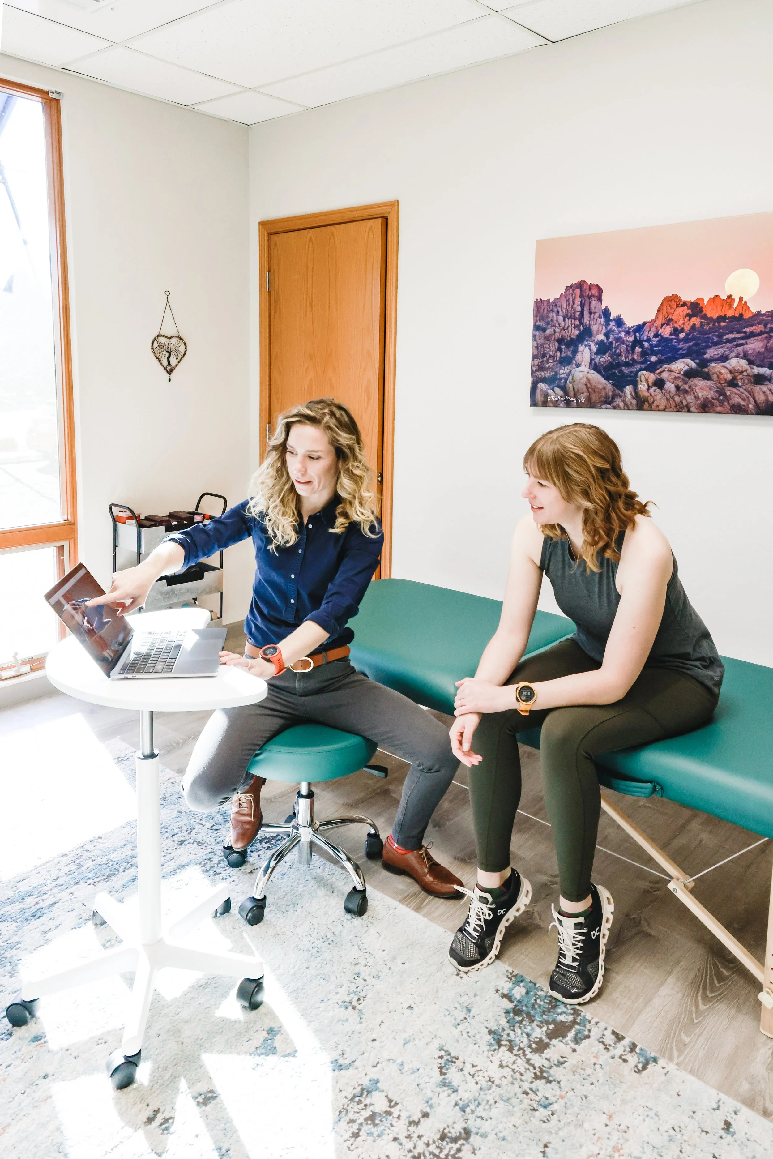 Two physical therapists sitting in a coaching session with one pointing at the computer for a demonstration.