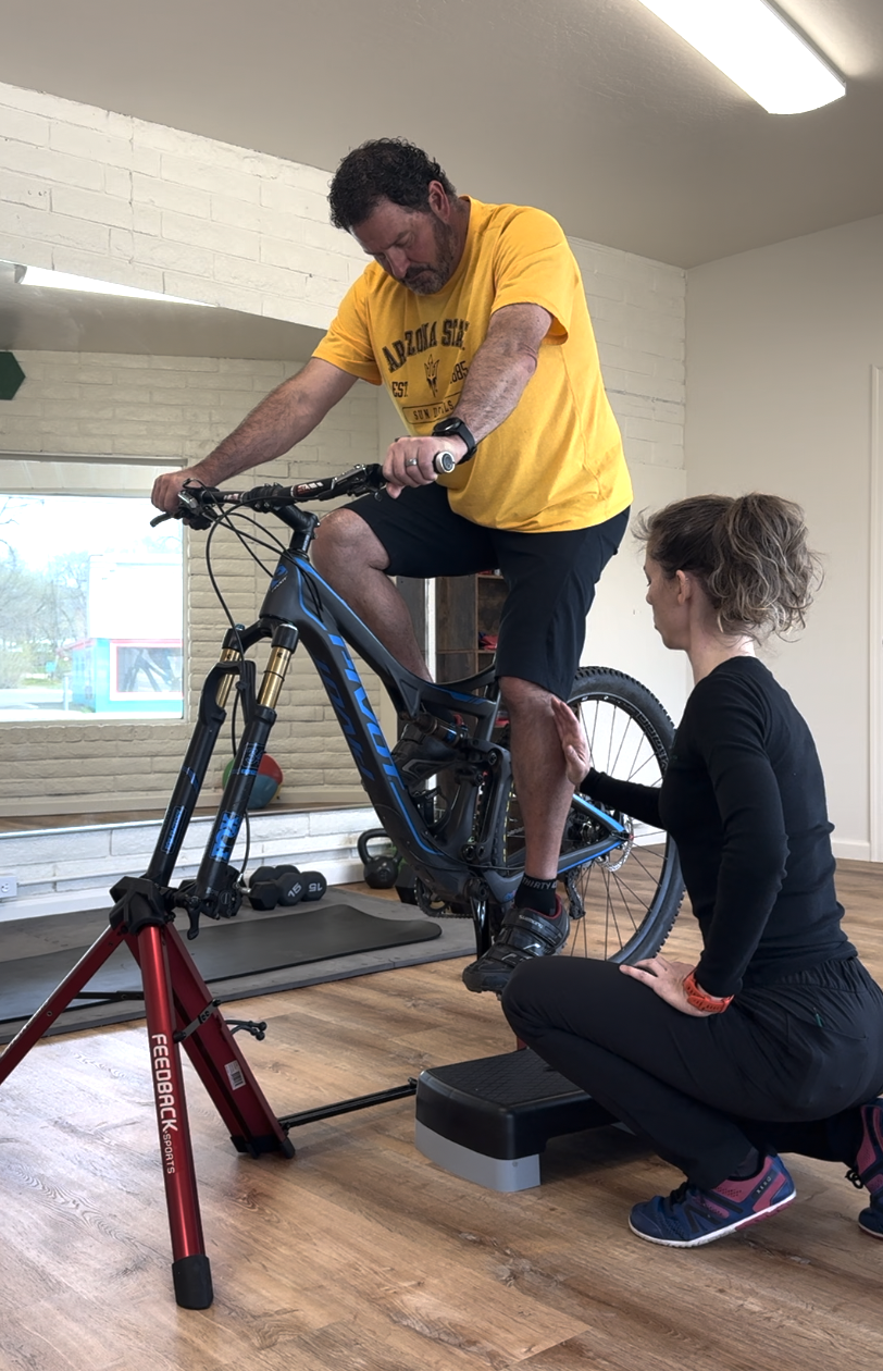 A physical therapist conducting a bike fit appointment with a client sitting on his bike