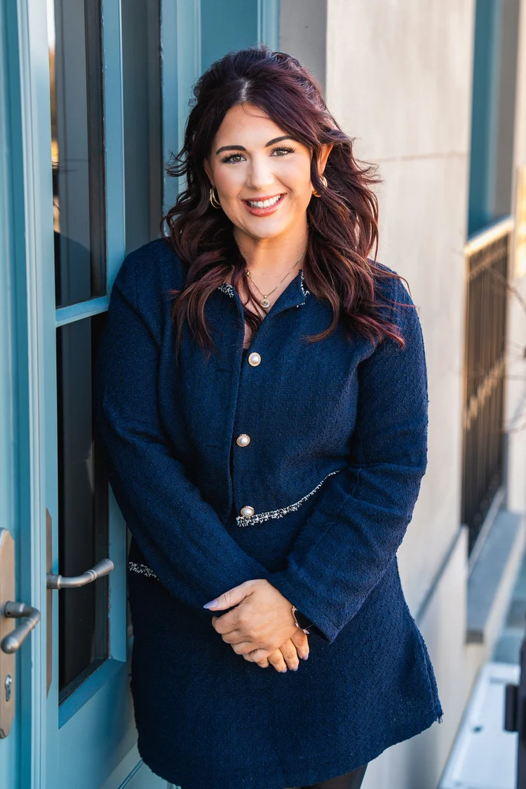 Smiling woman with long wavy hair in a navy tweed jacket leaning by a blue door, business branding portrait, Lake Charles