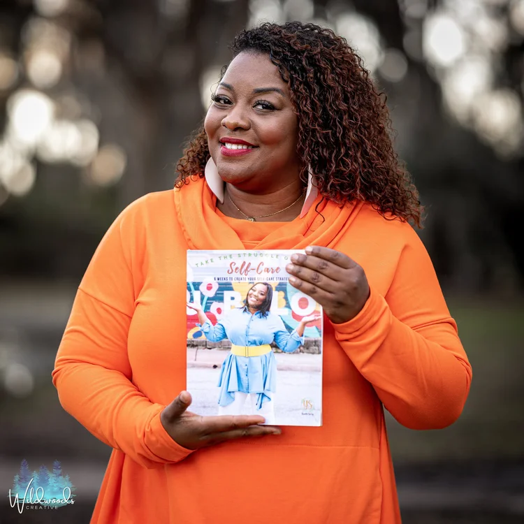 Smiling author in an orange sweater holding up her book outdoors, branding portrait