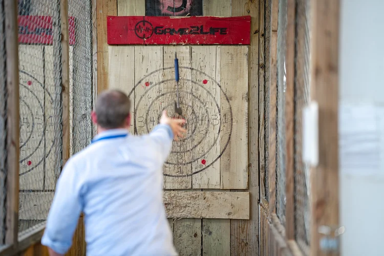 Man in a light blue shirt throwing an axe at a wooden bullseye target in a lane at an axe-throwing venue, business branding photo, Lake Charles