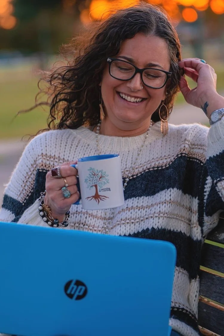 Smiling business owner with glasses holding a coffee mug while working on her laptop, branding photo