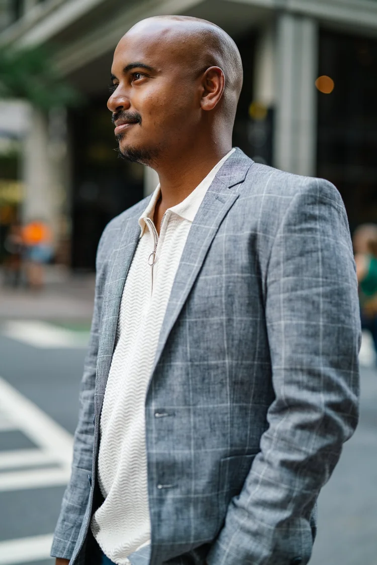 Bald man with a goatee in a gray plaid blazer and cream zip polo standing on a city street, branding portrait, Lake Charles