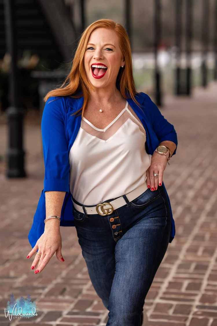 Laughing red-haired woman in a royal blue blazer and white top walking down a brick sidewalk, lifestyle branding portrait, Lake Charles