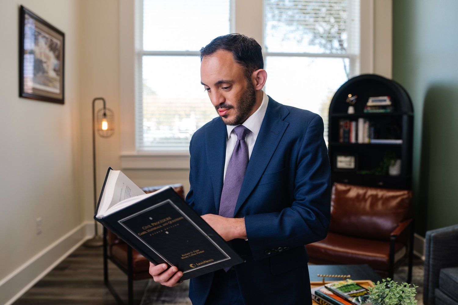 Business owner in a navy suit reading a law book in his sunlit Lake Charles office, branding photography by Wildwoods Creative
