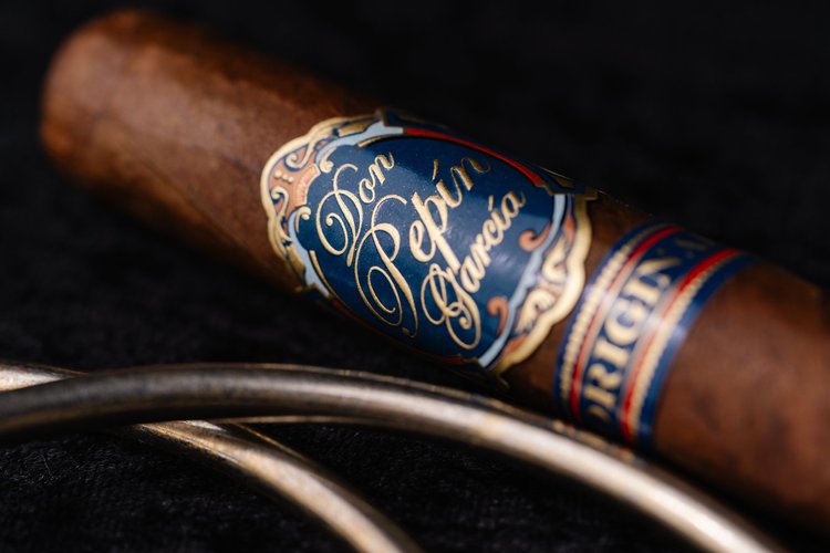 Close-up of a Don Pepin Garcia cigar with its blue and gold band on black fabric, product photo, Lake Charles