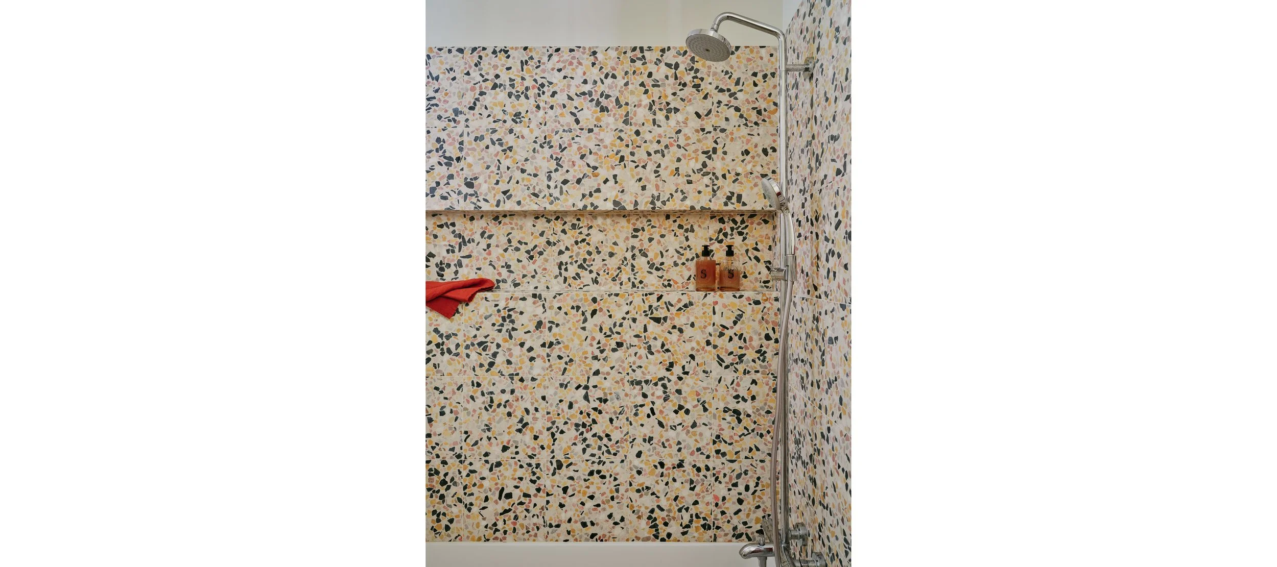 Shower with pebble tile walls, a rain shower head, a handheld shower head, two soap dispensers, and a red towel.