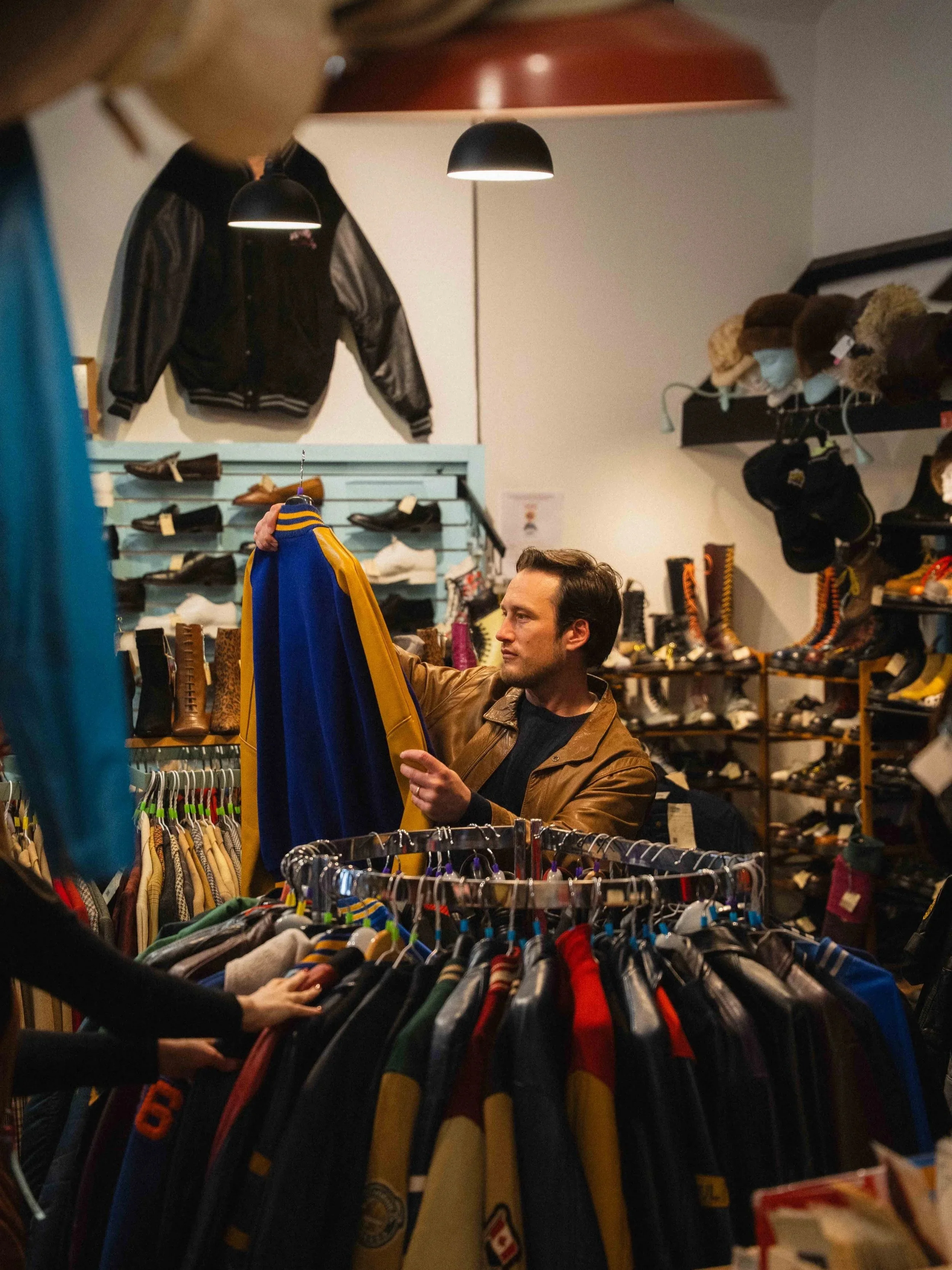 a man holding up a vintage letterman jacket while browsing a vintage clothing store