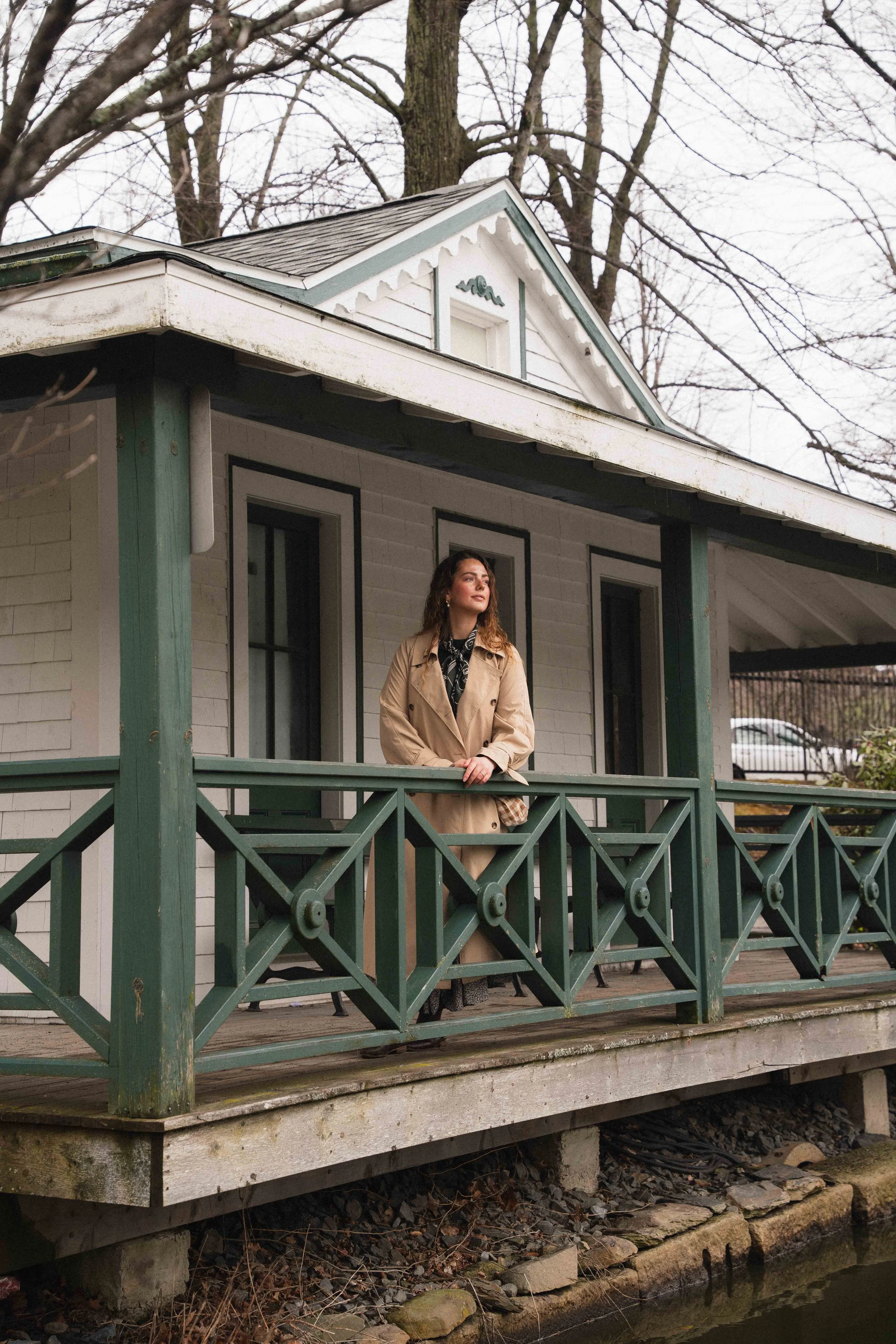 a woman in a trench coat and neck scarf looking out from a porch over a lake in the Halifax Public Gardens, a formal victorian garden in Canada, for a guide to Third Spaces